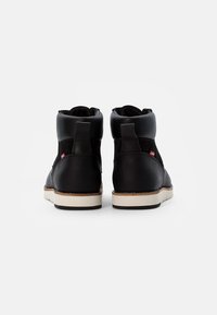 Zwarte hoge schoenen van soepel leer en synthetisch materiaal, met een witte rubberen zool en een klein logo-label aan de zijkant.