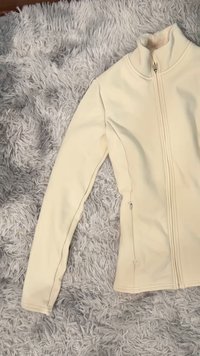 Kremowa bluza na zamek wykonana z miękkiego, teksturowanego materiału. Posiada wysoki kołnierz, dopasowany krój oraz kieszeń z zamkiem po boku.