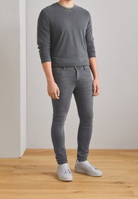 Camisa gris de manga larga combinada con jeans skinny grises y zapatillas blancas. Textura suave, ajuste ceñido, diseño casual y esquema de color monocromático.