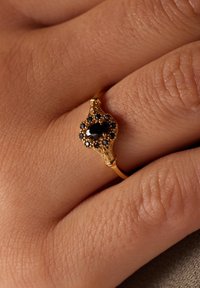 Bague en or ornée d'une pierre noire ovale entourée de petites pierres noires, avec des détails ornés sur le bandeau.
