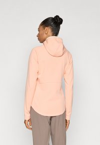 Φούτερ με κουκούλα από απαλό ύφασμα χρώματος ροδάκινου. Διαθέτει καμπυλωτό τελείωμα και εφαρμοστά μανίκια. Το πίσω μέρος έχει ραφές για σχέδιο και άνετη εφαρμογή.