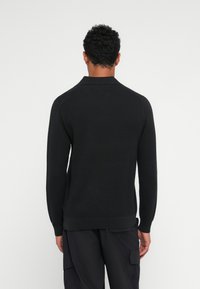 Sort strikket sweater med krave, ribbet tekstur og lange ærmer. Enkel design med tætsiddende pasform og ensfarvet. 