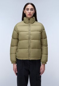 Olivgrön pufferjacka med hög krage, full dragkedja fram, elastiska ärmslut och en boxig silhuett. Texturerat quiltat mönster.