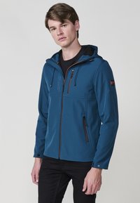 Giacca softshell blu con cappuccio, tasche con zip, cerniere marroni a contrasto e una texture liscia. Presenta cordini regolabili.