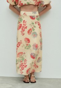 Maxi-Rock aus leichtem beigem Stoff mit einem floralen Druck in Rot, Blau und Grün, mit einer glatten Textur und einem figurschmeichelnden Taillenbund.