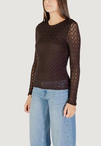 Top in pizzo nero a maniche lunghe con motivo a zigzag e scollatura rotonda, abbinato a jeans a gamba ampia blu chiaro.