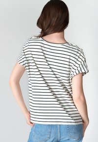 Camiseta blanca de manga corta con rayas negras horizontales, cuello redondo y corte relajado. Combinada con pantalones cortos de mezclilla azul claro.