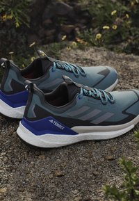 Blue and black outdoor shoes feature a textured upper, contrasting accents, and a responsive white sole. Design includes a Gore-Tex label.