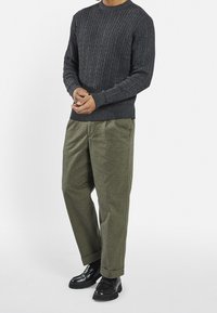 Pull tricoté gris foncé avec une texture côtelée et un col rond, associé à un pantalon ample de couleur vert olive et des chaussures noires.