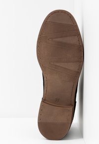Semelle en caoutchouc marron avec des motifs de grip texturés, des bords cousus et une indication de taille 37. La chaussure est présentée sur un fond blanc.