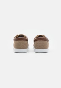 Brown canvas sneakers with dark brown accents and white soles, featuring a textured surface and rear pull tabs for easy wear.