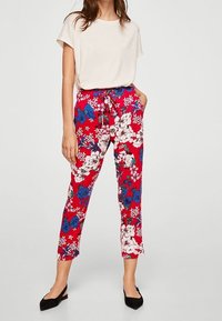 Pantalons floraux rouges avec motifs de fleurs bleues et blanches, dotés d'une taille élastique et de poches avant. Associés à un haut beige clair.