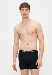 Černé boxerky z bavlny s elastickým páskem s logem značky. Střih je přiléhavý, s hladkou texturou a minimem detailů.