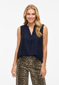 Top sin mangas de color marino con escote en V y detalle de pliegue, combinado con pantalones de estampado de leopardo en tonos beige, confeccionados en tejido ligero.
