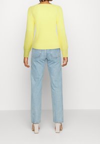 Ljusgul stickad tröja med långa ärmar, tillsammans med ljusblå högmidjade jeans och beige klackskor med blockklack.