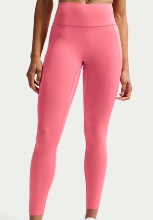 Kobieta ubrana w bezszwowe, jasnoróżowe legginsy z wysokim stanem, stojąca ze zrelaksowanymi rękami wzdłuż ciała na tle jednolitym.