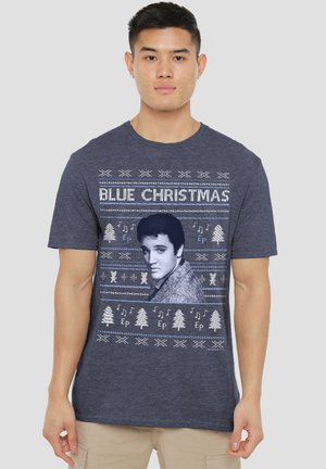 Mann trägt ein marineblaues "Blue Christmas"-T-Shirt mit einem schwarz-weißen Porträt von Elvis Presley sowie weihnachtlichen Mustern und musikalischen Noten.
