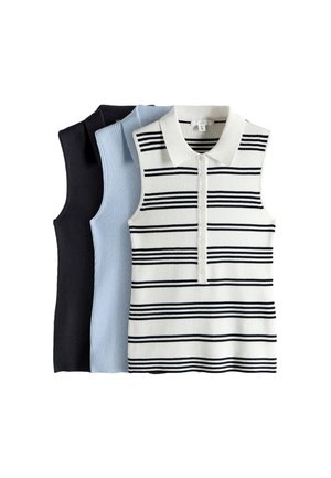 Giovane donna con lunghi capelli castani che indossa un top nero senza maniche, pantaloni neri e una cintura, seduta su un cubo bianco su uno sfondo chiaro.