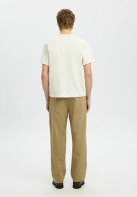 Off-white tričko s krátkým rukávem a rovný střih, zkombinované s širokými kalhotami v odstínu tan. Obě části jsou vyrobeny z měkké, lehké tkaniny.
