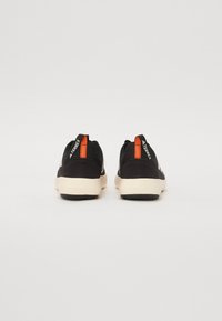 Svarta sneakers med en strukturerad överdel, beige mellansula och svart yttersula. Har orangea detaljer på hälen och branding på flikarna.