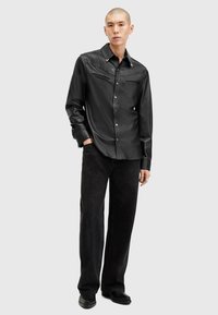 Svart skinnskjorte med knappestolpe og spiss krage, samt brystlommer og hvite detaljer. Kombinert med løstsittende svarte jeans og svarte sko.