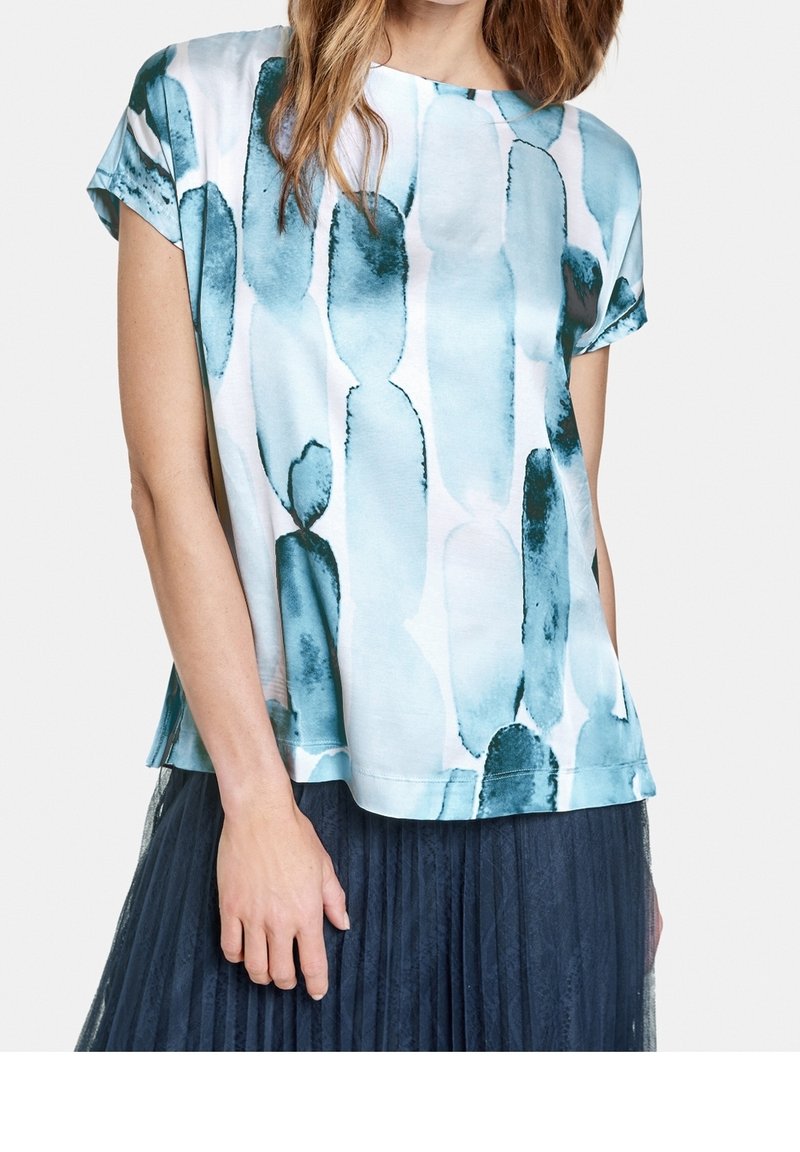 Top de manga corta en azul claro con manchas abstractas en azul oscuro, hecho de una tela suave. Presenta un escote redondeado y corte relajado.