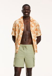 Korte mouw bloemenhemel in geel en oranje, gecombineerd met lichtgroene cargoshorts met zijzakken. Gladde stof met een relaxte pasvorm.