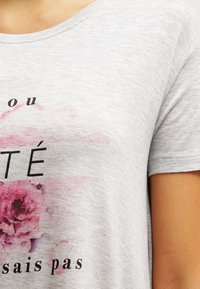 T-shirt in cotone grigio con scollatura rotonda, maniche corte e stampa floreale rosa con testo nero. Design casual con una texture morbida.