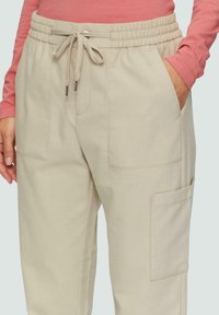 Beige sweats met een zachte textuur, elastische tailleband, trekkoordsluiting en grote zijzakken. Heeft subtiele stikdetails.