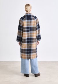 Long plaid coat featuring blue, brown, and beige colors, designed with a loose fit and wide sleeves. Paired with light blue wide-leg jeans.