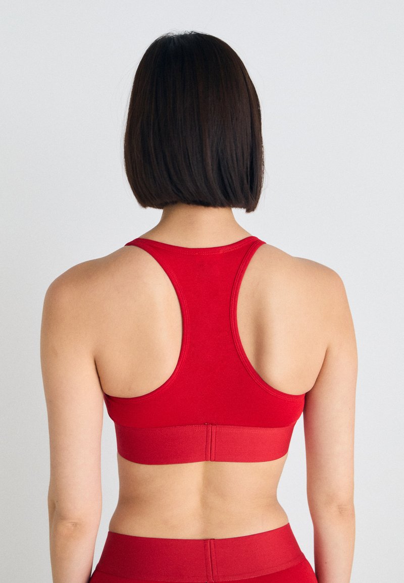 Bra sportivo rosso con un design aerodinamico, stile racerback e fascia elastica in basso. Texture liscia e colore uniforme.