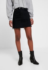 Czarna jeansowa spódnica o prostym kroju, z postrzępionym dołem i przednimi kieszeniami, w połączeniu z szarym hoodie i czarnymi botkami za kostkę.