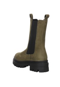 Bottine Chelsea en daim vert olive avec panneau latéral élastique noir, semelle épaisse à crampons noire, et languettes de traction en haut à l'arrière et à l'avant.