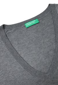 Szary dzianinowy sweter z dekoltem w kształcie litery V i ściągaczami na brzegach. Metka z napisem "United Colors of Benetton" w zielonym prostokącie. Miękka faktura.
