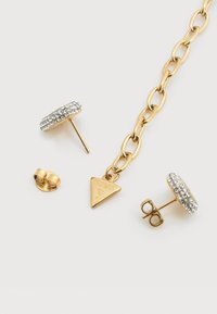 Σετ κοσμημάτων με χρυσή απόχρωση που περιλαμβάνει λαμπερά στρογγυλά σκουλαρίκια με στρας και αλυσίδα με τρίγωνο μενταγιόν.