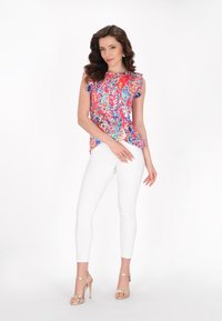 Mønstret ærmeløs bluse med flæse detaljer, parret med hvide skinny jeans og metallic guld højhælede sko. Glat stofstruktur.