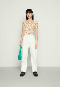 Blusa creme com padrão floral e decote franzido, calças brancas de cintura alta, bolsa verde e sapatos plataforma pretos.