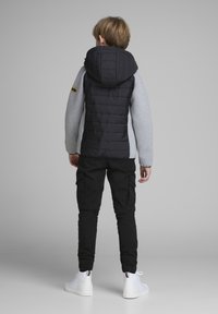 Padded black vest with gray sleeves, featuring a hood. Paired with black cargo pants and white sneakers, viewed from the back.