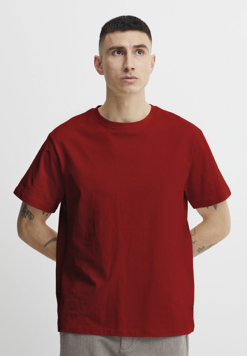 Maroon short-sleeve t-shirt, round neckline, plain texture, standard fit. Notable tattoos visible on the arms.