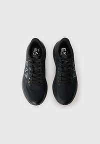 Black athletic sneakers with a mesh upper, smooth sole, and flat laces. Features a logo on the outer side and ventilation holes throughout.