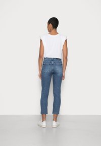 Jeans de mezclilla azul de tiro alto y ajuste slim, con un dobladillo deshilachado y dos bolsillos traseros, combinados con una blusa sin mangas blanca.