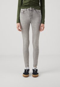 Jeans skinny gris claro con un diseño desgastado, que cuentan con cinco bolsillos y pasadores para cinturón, combinados con zapatillas negras y blancas.