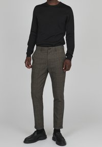 Svart långärmad skjorta som är ihopparad med bruna rutiga byxor. Byxorna har en slim fit och knappstängning. Svarta skor fulländar outfiten.