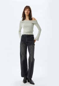 Lichtgrijze off-shoulder lange mouwen top, met textuur. Hooggewaisted zwarte wijde pijpen jeans, vervaagd met vijf zakken. Zwarte puntige enkellaarzen.