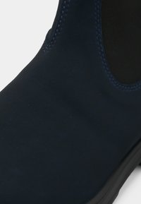 Zbliżenie na ciemnoniebieski zamszowy botek za kostkę z czarną elastyczną wkładką boczną i czarną podeszwą.