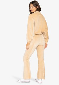Beige corduroy twee-delig set met een losse top met uitlopende mouwen en aangesloten flared broek, gecombineerd met witte sneakers.