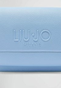 Portafoglio azzurro chiaro realizzato in materiale testurizzato, con logo incastonato "LIU·JO MILANO" e cuciture decorative lungo i bordi.