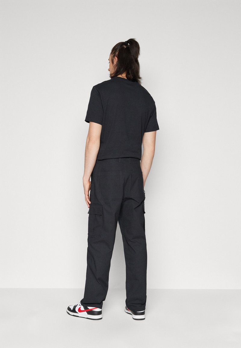 T-shirt en coton noir et pantalon cargo avec poches. La tenue présente une coupe décontractée, associée à des baskets noires et blanches.