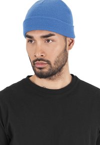 Berretto di lana blu a maglia con una vestibilità aderente, caratterizzato da una trama a coste verticali; indossato con una maglietta nera semplice.