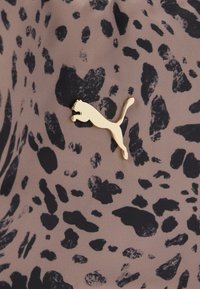 Λογότυπο Puma σε χρυσό χρώμα πάνω σε ύφασμα ταουπ με μαύρο αφηρημένο μοτίβο λεοπάρδαλης.